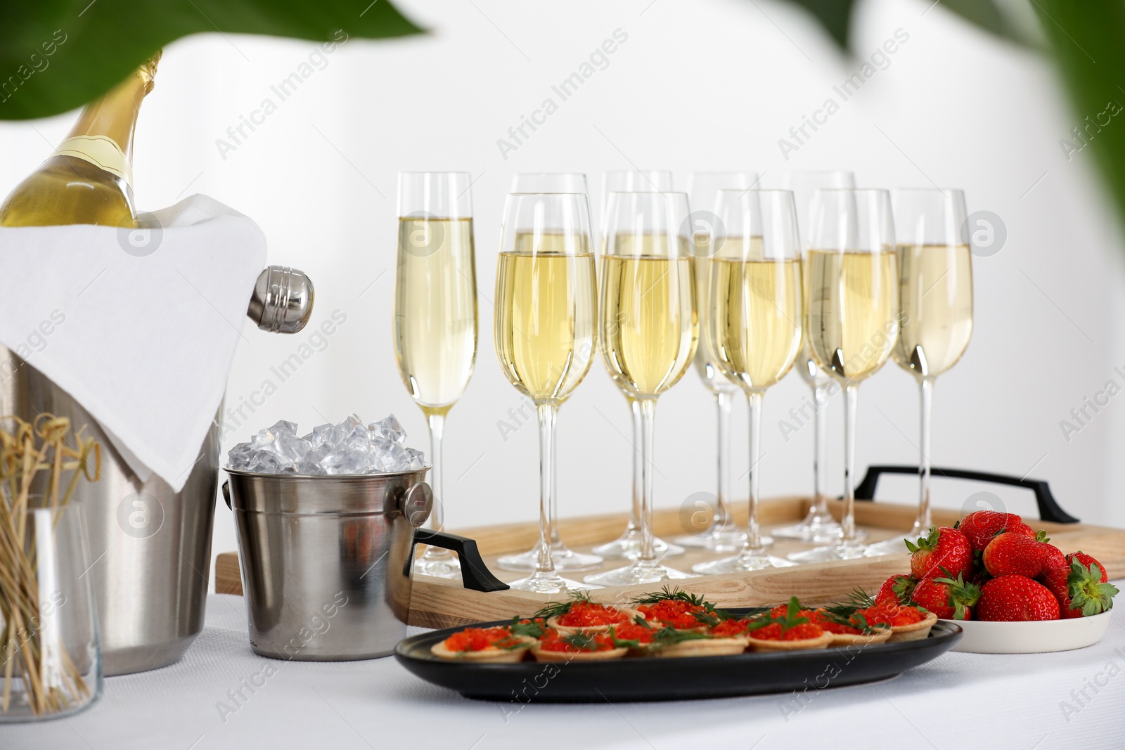 Photo of Champagne, ice bucket, strawberries and canapes with red caviar on white table indoors