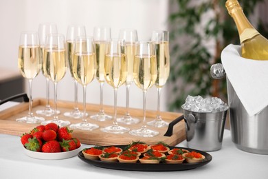 Photo of Champagne, ice bucket, strawberries and canapes with red caviar on white table indoors