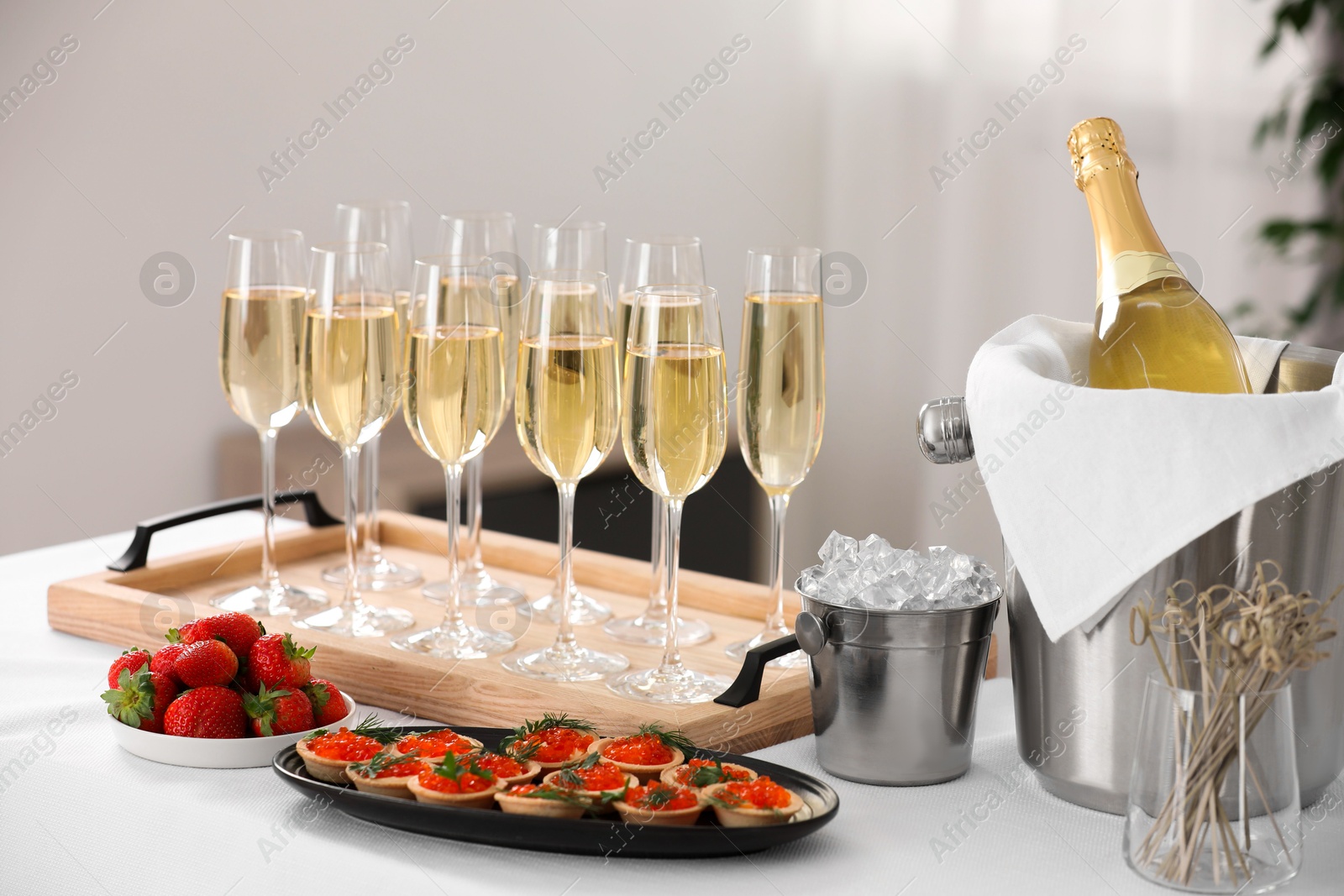 Photo of Champagne, ice bucket, strawberries and canapes with red caviar on white table indoors