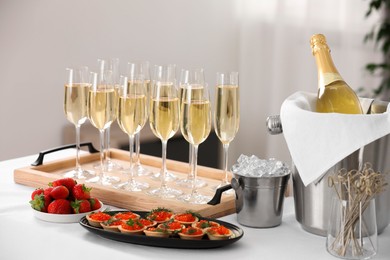 Photo of Champagne, ice bucket, strawberries and canapes with red caviar on white table indoors