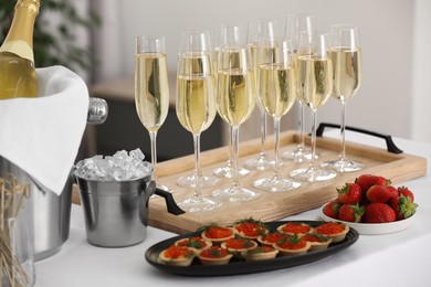 Photo of Champagne, ice bucket, strawberries and canapes with red caviar on white table indoors