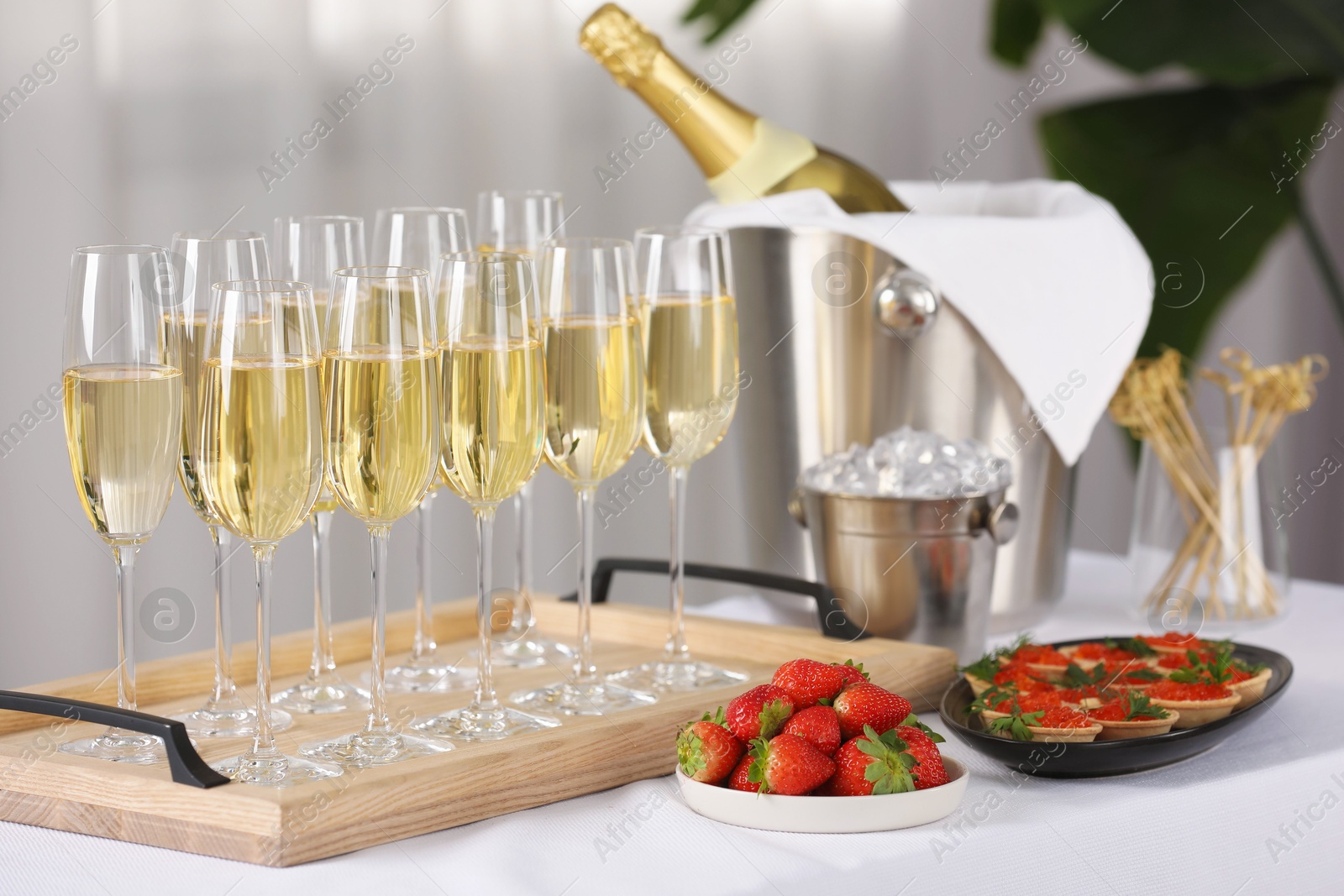 Photo of Champagne, ice bucket, strawberries and canapes with red caviar on white table indoors