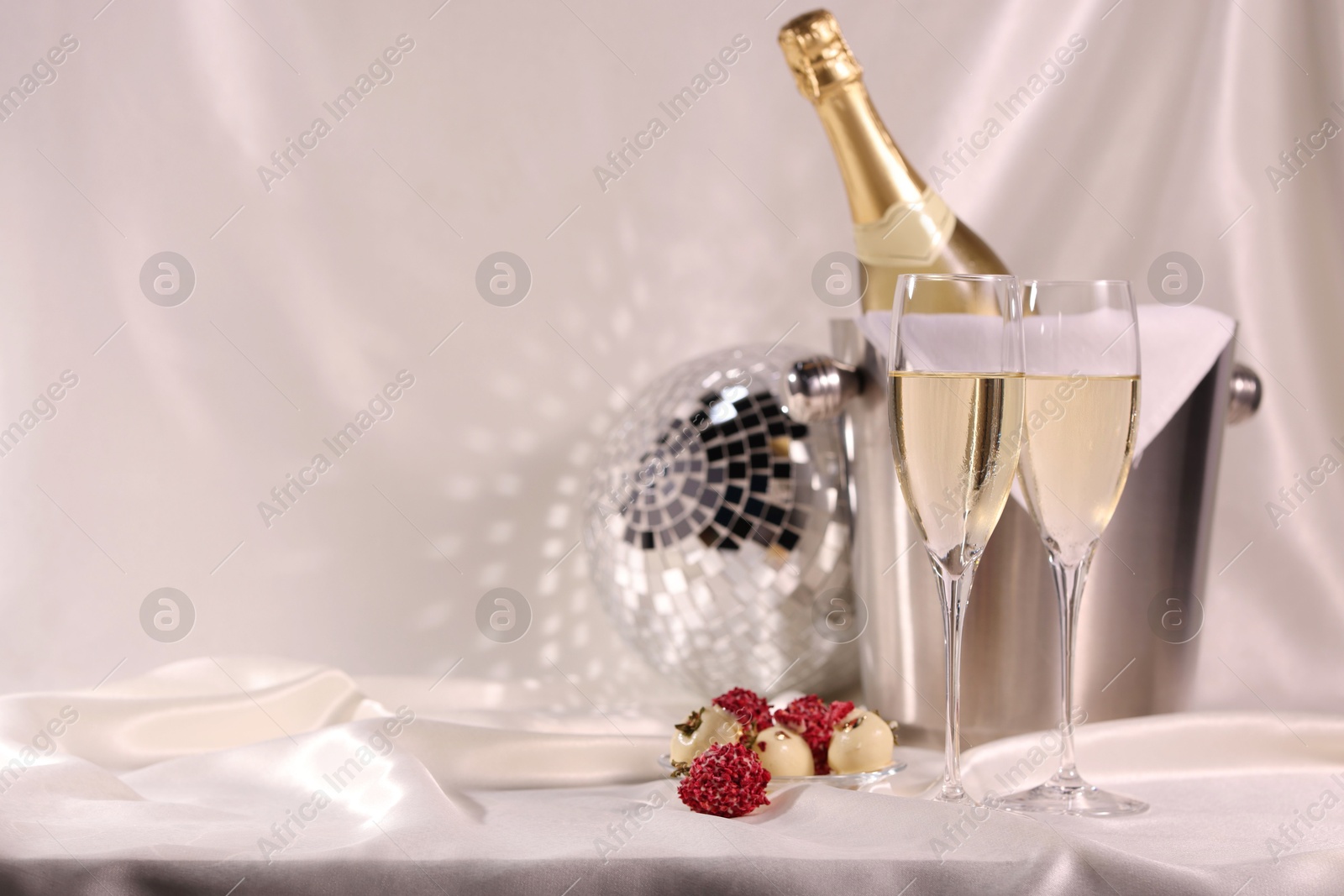 Photo of Champagne in glasses, ice bucket with bottle and tasty candies on white fabric, space for text