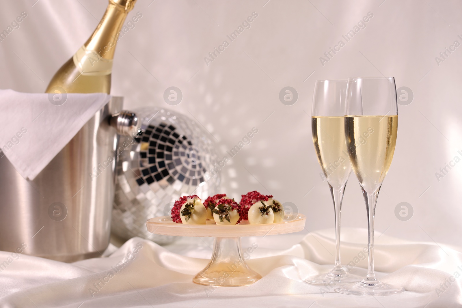 Photo of Champagne in glasses, ice bucket with bottle and tasty candies on white fabric