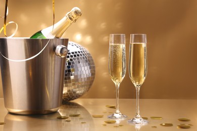 Photo of Champagne in glasses and ice bucket with bottle on golden background