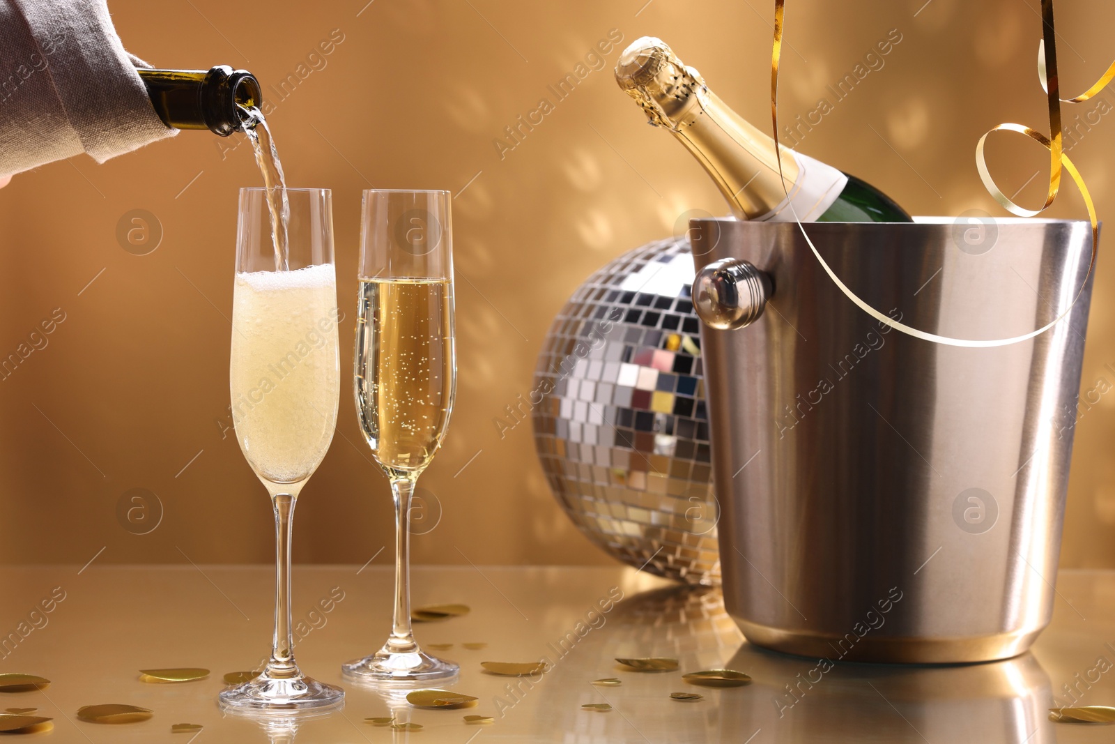 Photo of Pouring champagne into glass against golden background, closeup