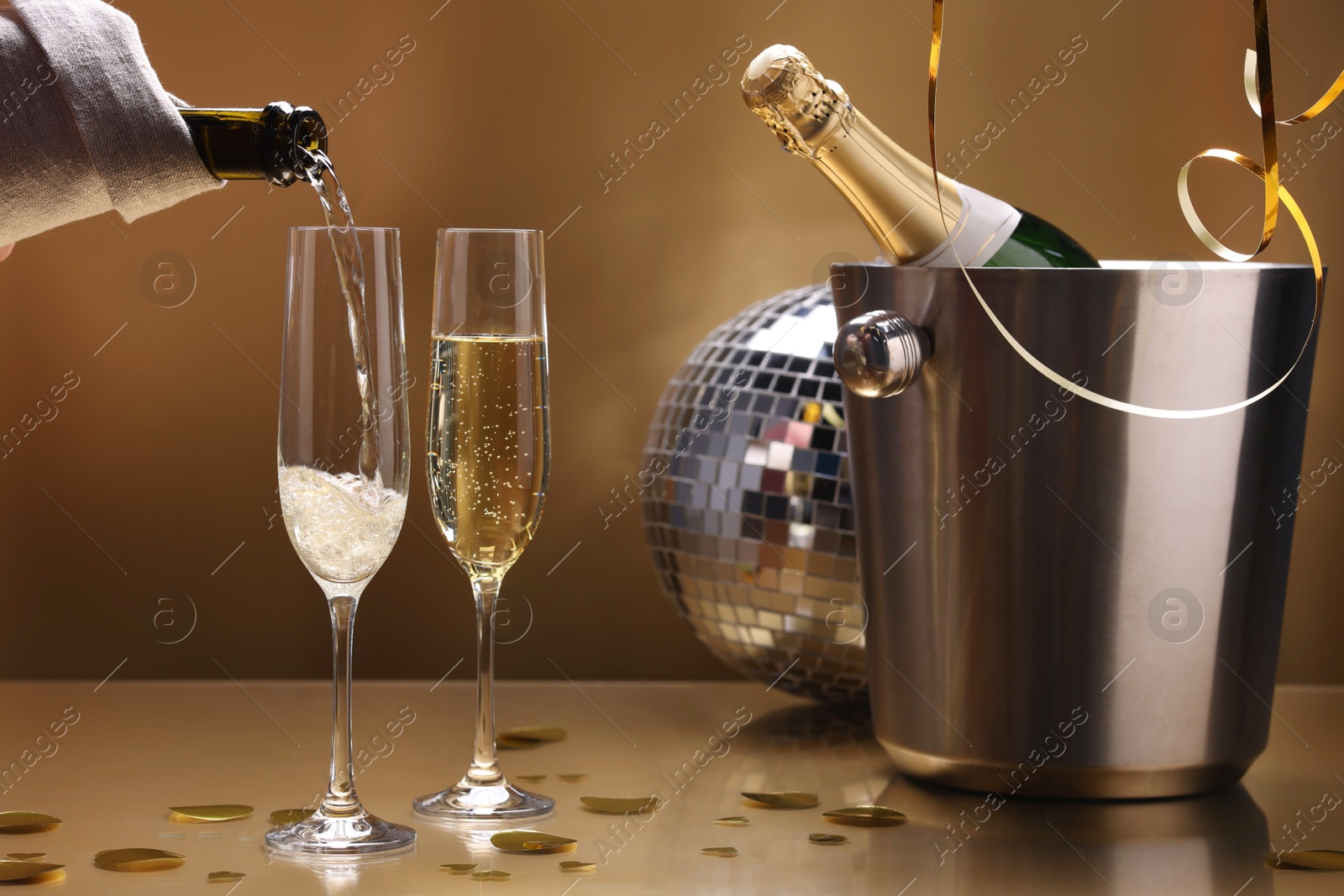 Photo of Pouring champagne into glass against golden background, closeup