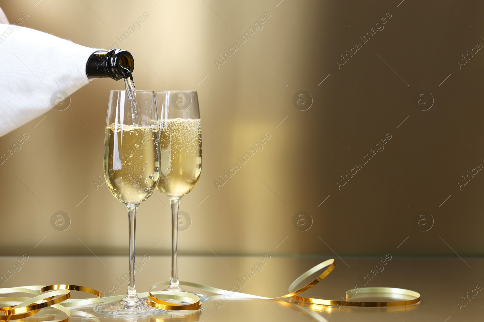 Photo of Pouring champagne into glass against golden background, closeup. Space for text