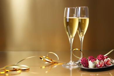 Photo of Champagne in glasses and tasty candies on golden background, space for text