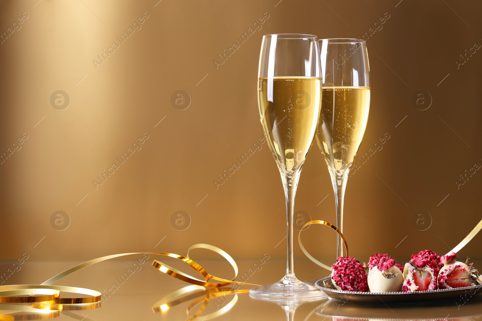 Photo of Champagne in glasses and tasty candies on golden background, space for text