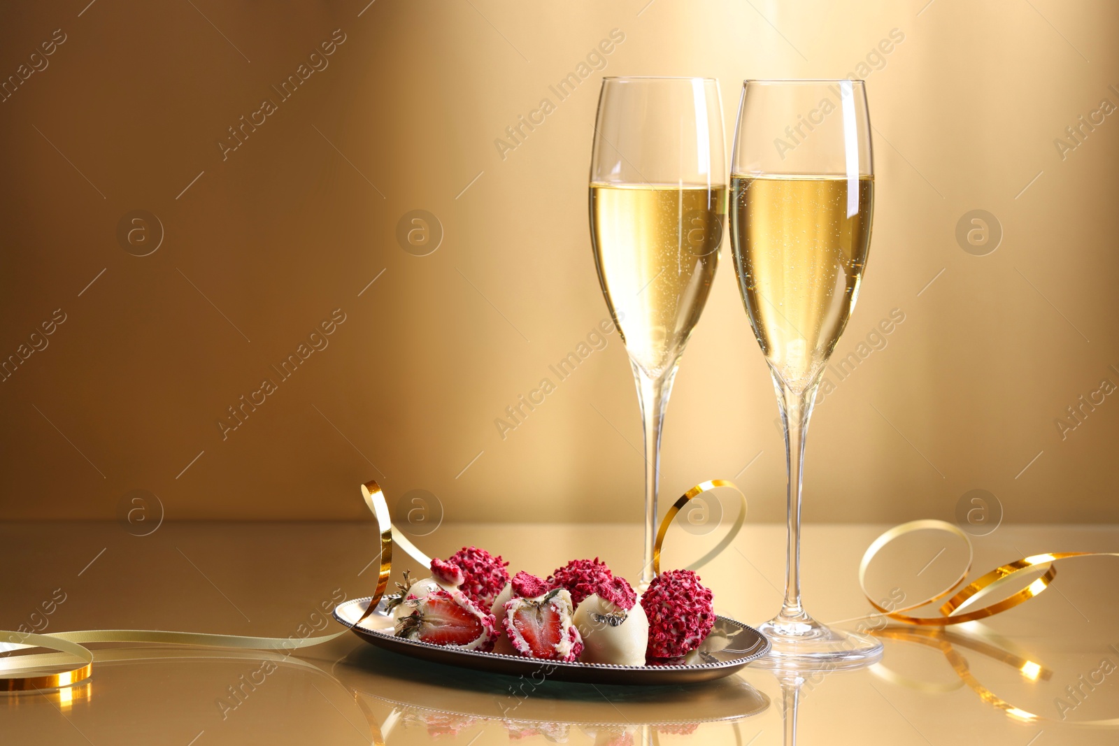 Photo of Champagne in glasses and tasty candies on golden background, space for text