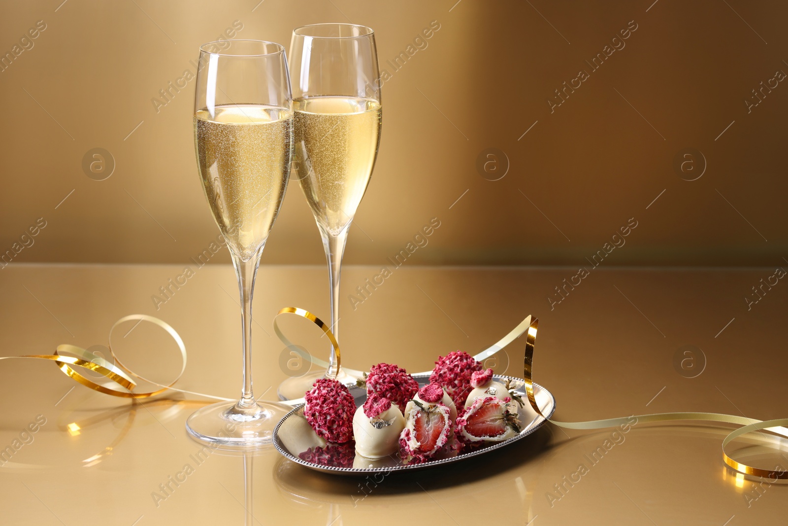 Photo of Champagne in glasses and tasty candies on golden background, space for text