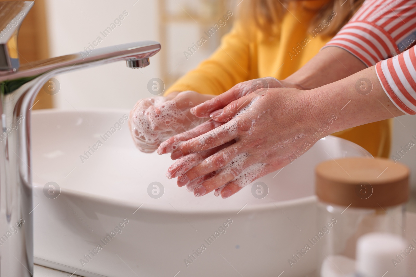 Photo of Mother and daughter washing their hands above sink indoors, closeup