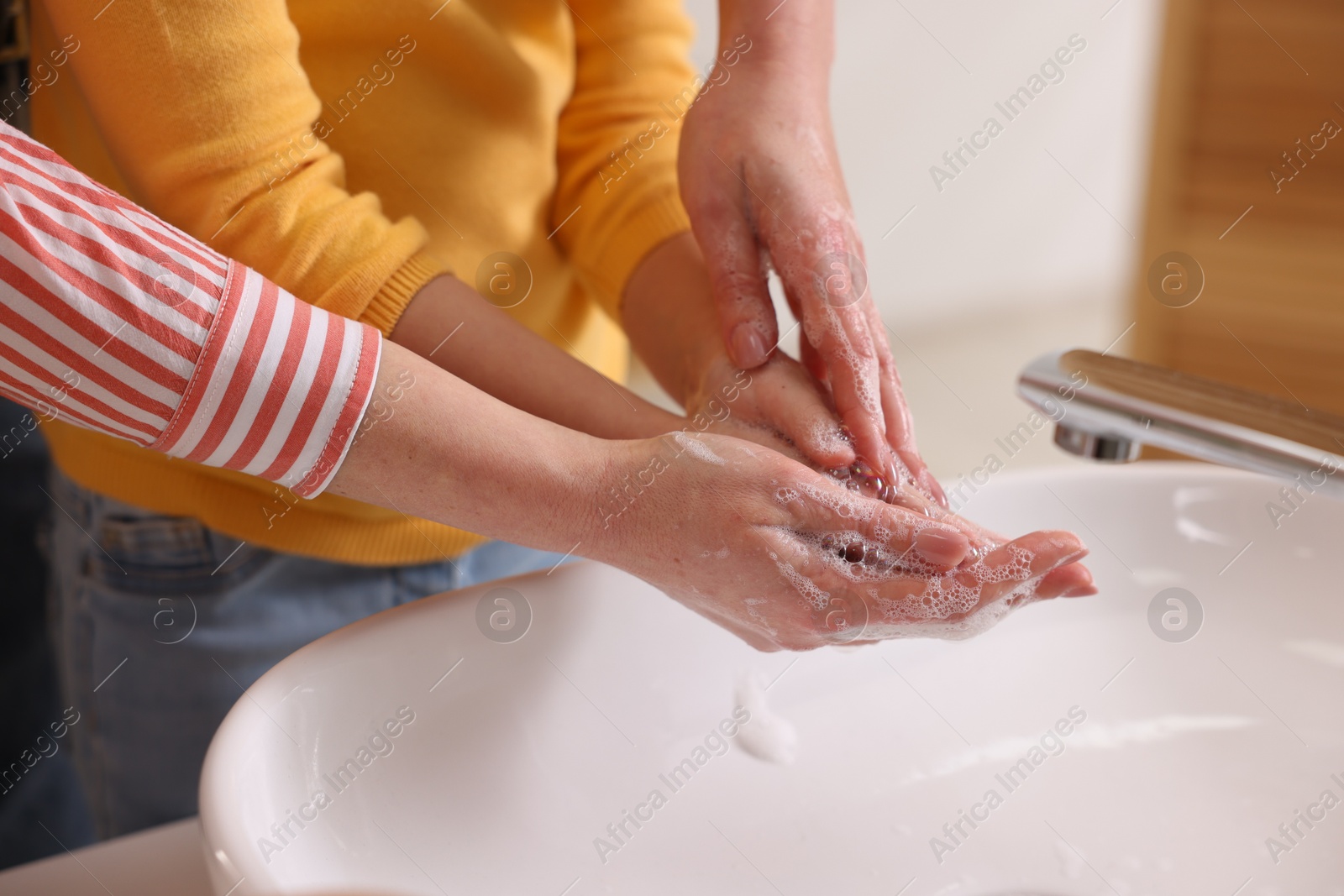 Photo of Mother and daughter washing their hands above sink indoors, closeup