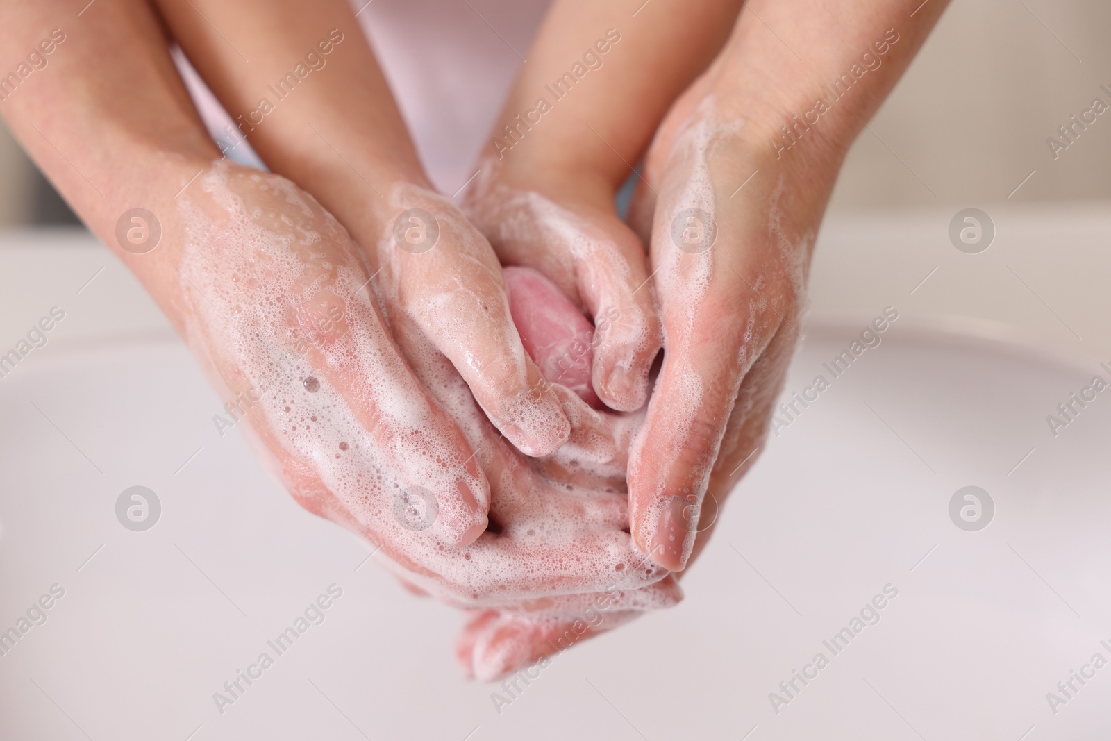 Photo of Mother and daughter washing their hands above sink indoors, closeup