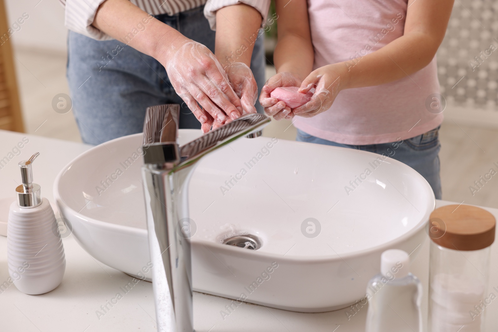 Photo of Mother and daughter washing their hands indoors, closeup