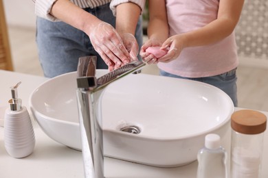 Photo of Mother and daughter washing their hands indoors, closeup