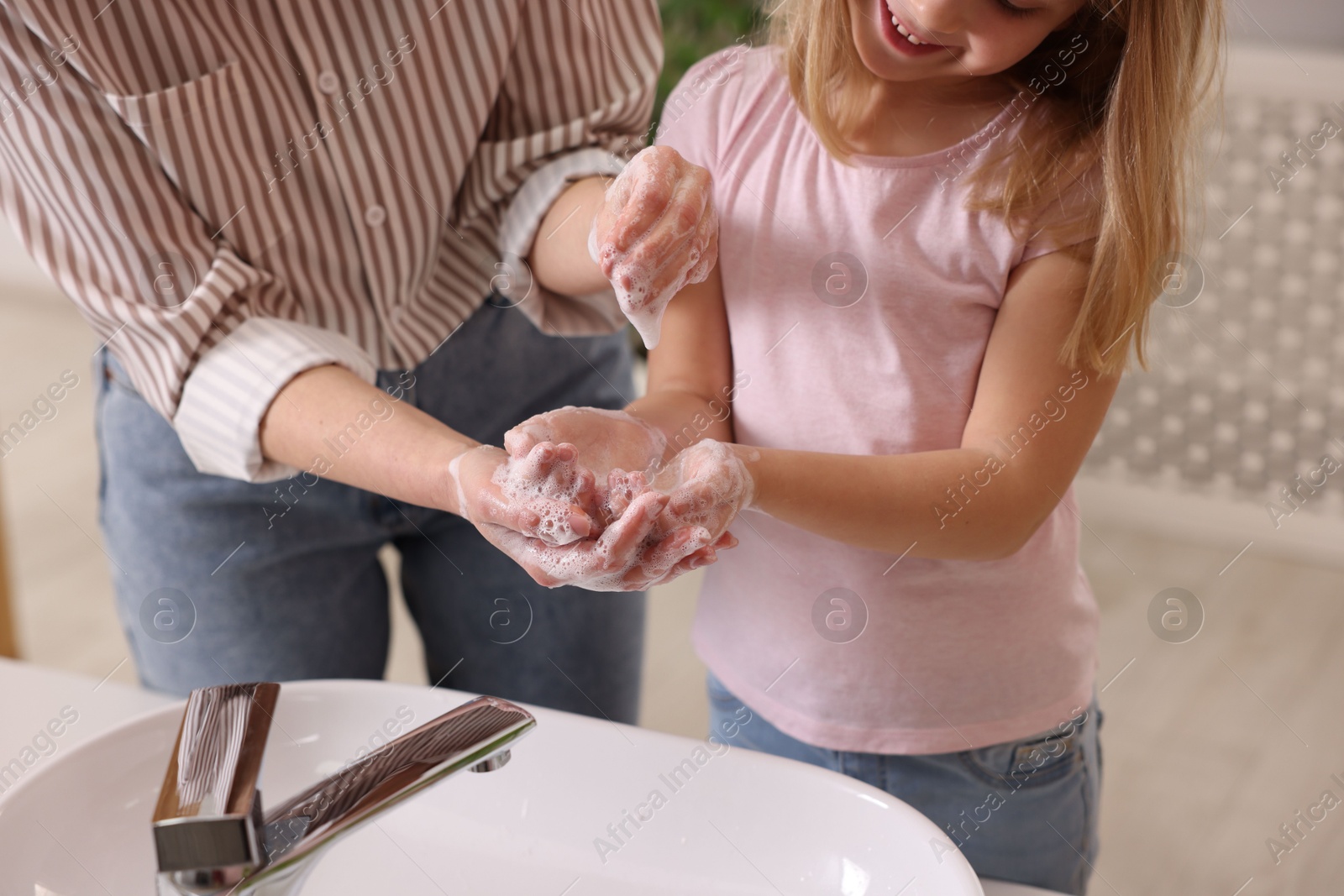 Photo of Mother and daughter washing their hands indoors, closeup