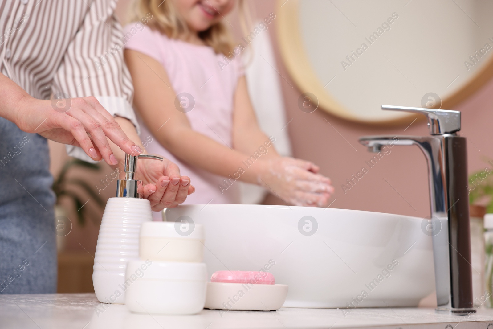 Photo of Mother and daughter washing their hands indoors, closeup