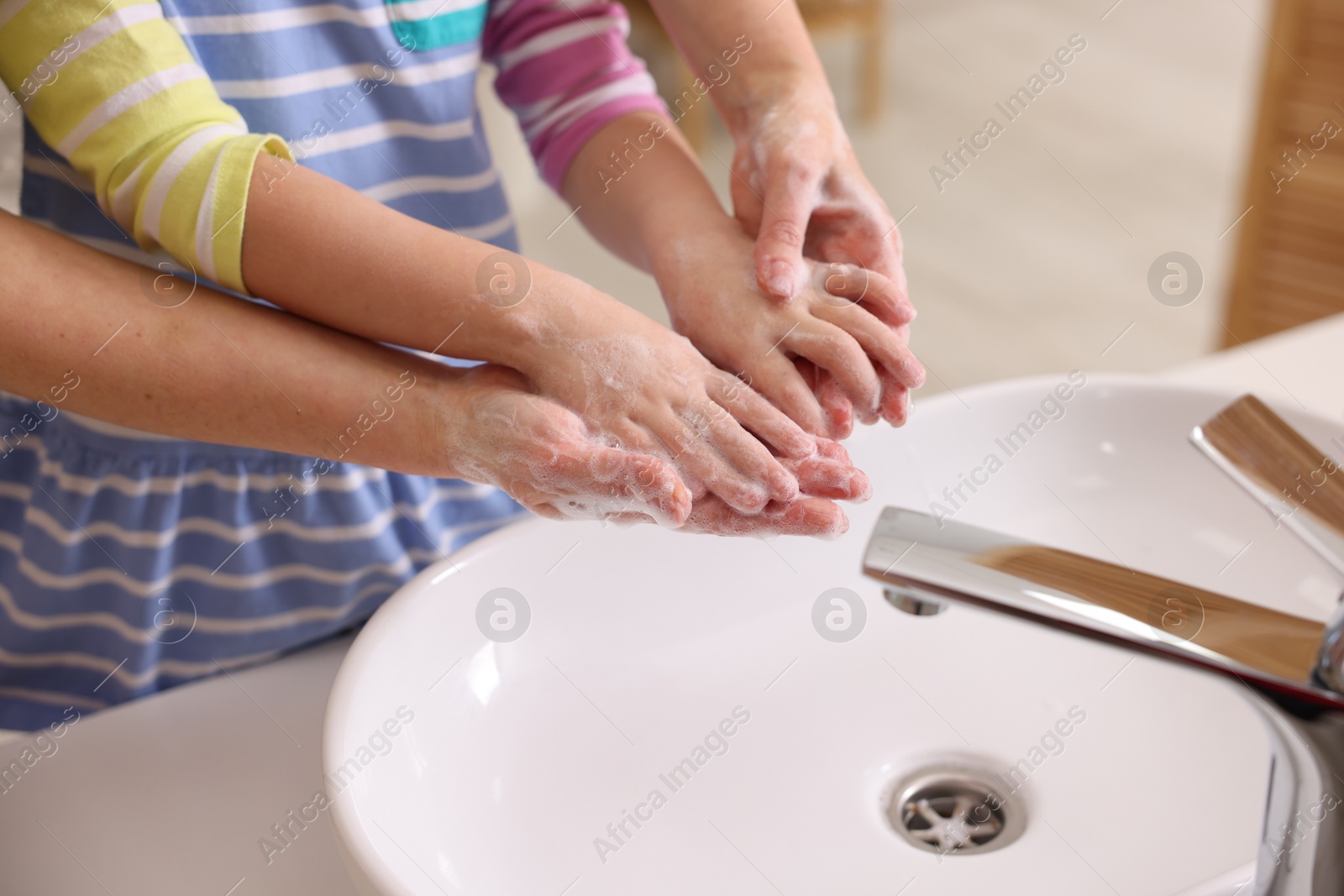 Photo of Mother and daughter washing their hands above sink indoors, closeup