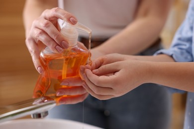 Photo of Mother and daughter washing their hands indoors, closeup