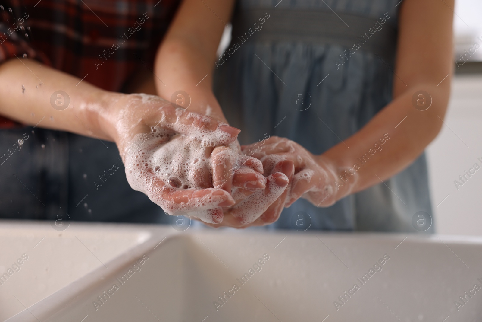 Photo of Mother and daughter washing their hands above sink indoors, closeup