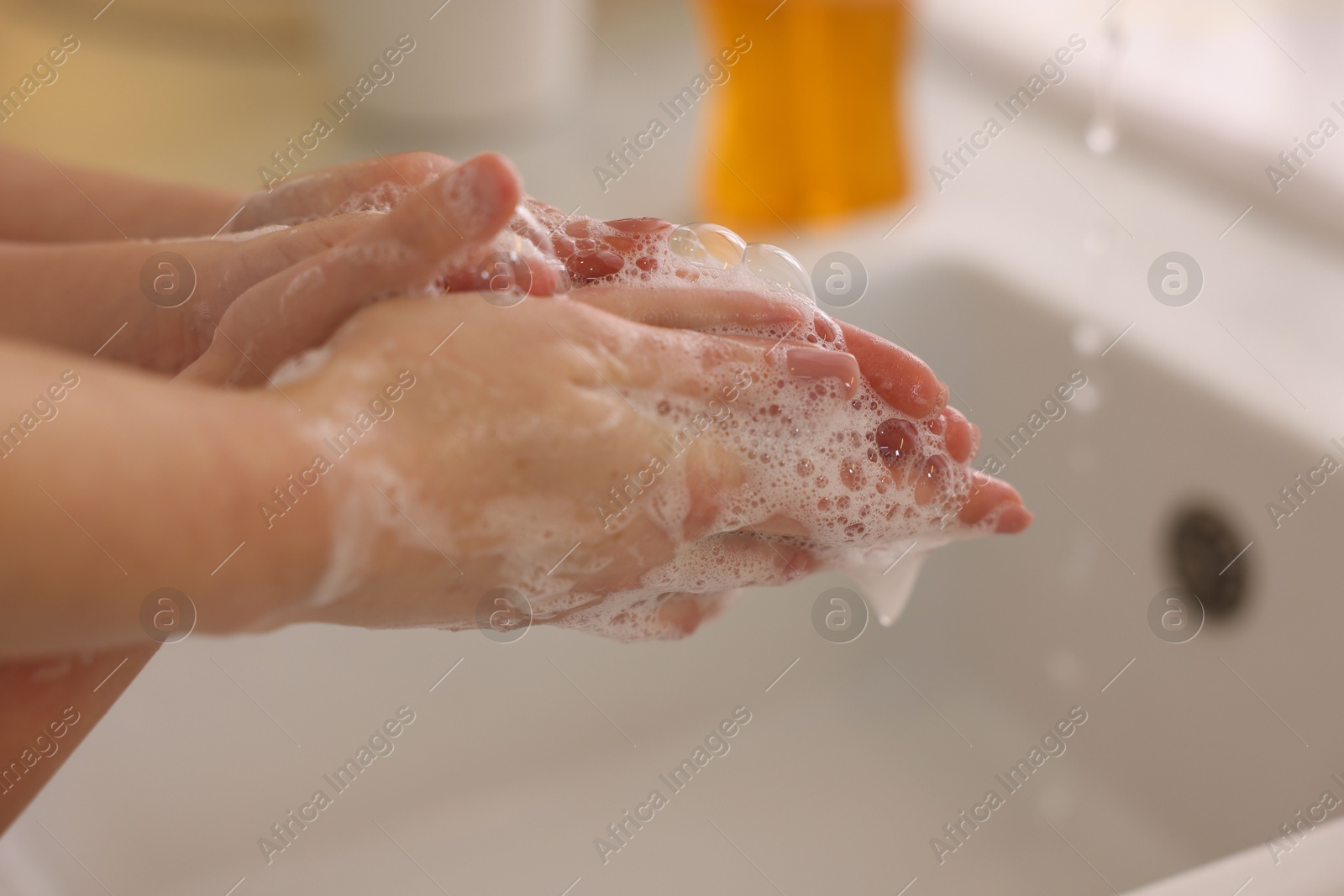 Photo of Mother and daughter washing their hands indoors, closeup