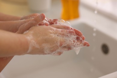 Photo of Mother and daughter washing their hands indoors, closeup