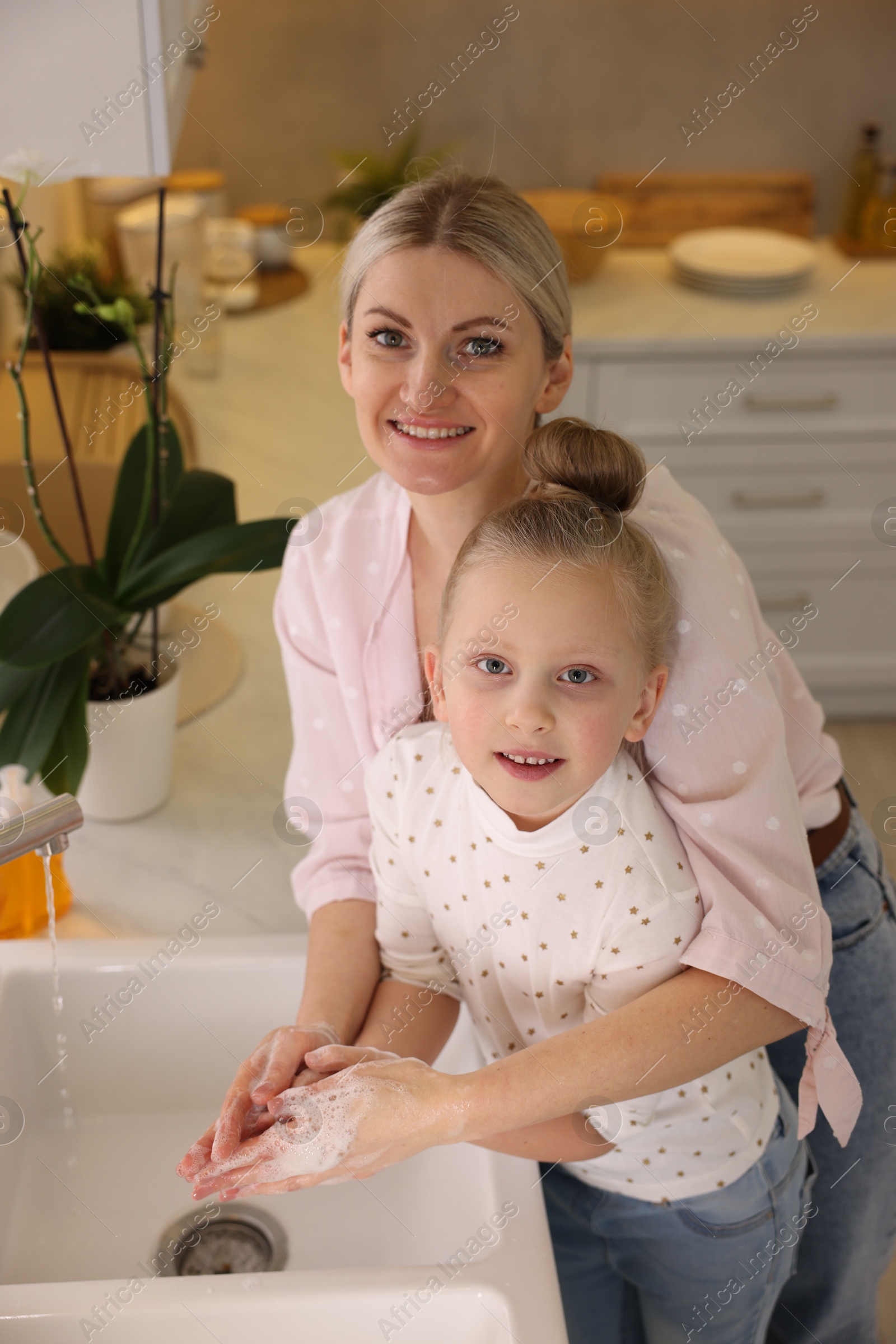 Photo of Happy mother and daughter washing their hands in kitchen