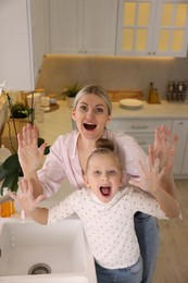 Photo of Happy mother and daughter washing their hands in kitchen