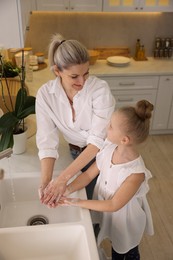 Photo of Happy mother and daughter washing their hands in kitchen