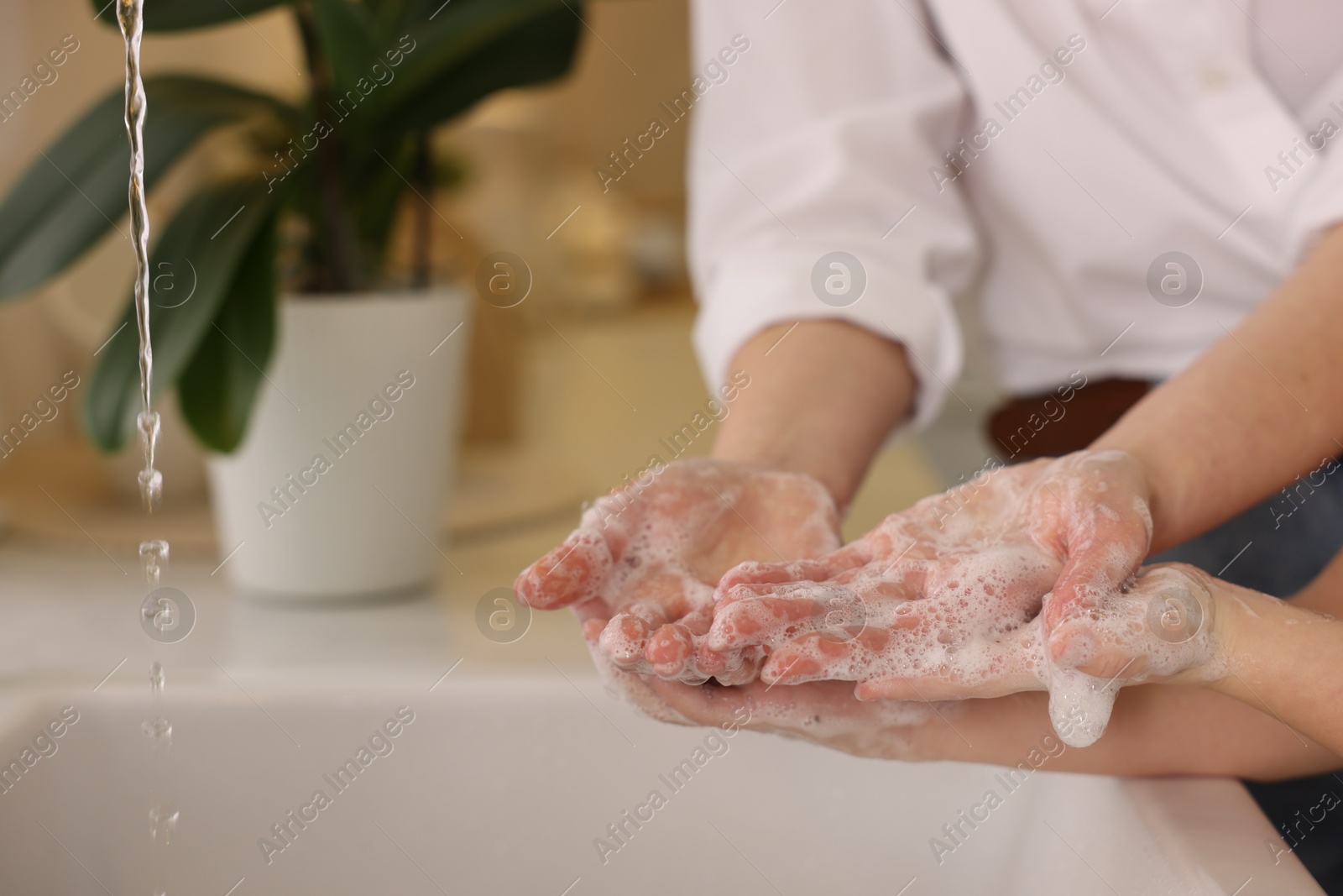 Photo of Mother and daughter washing their hands indoors, closeup