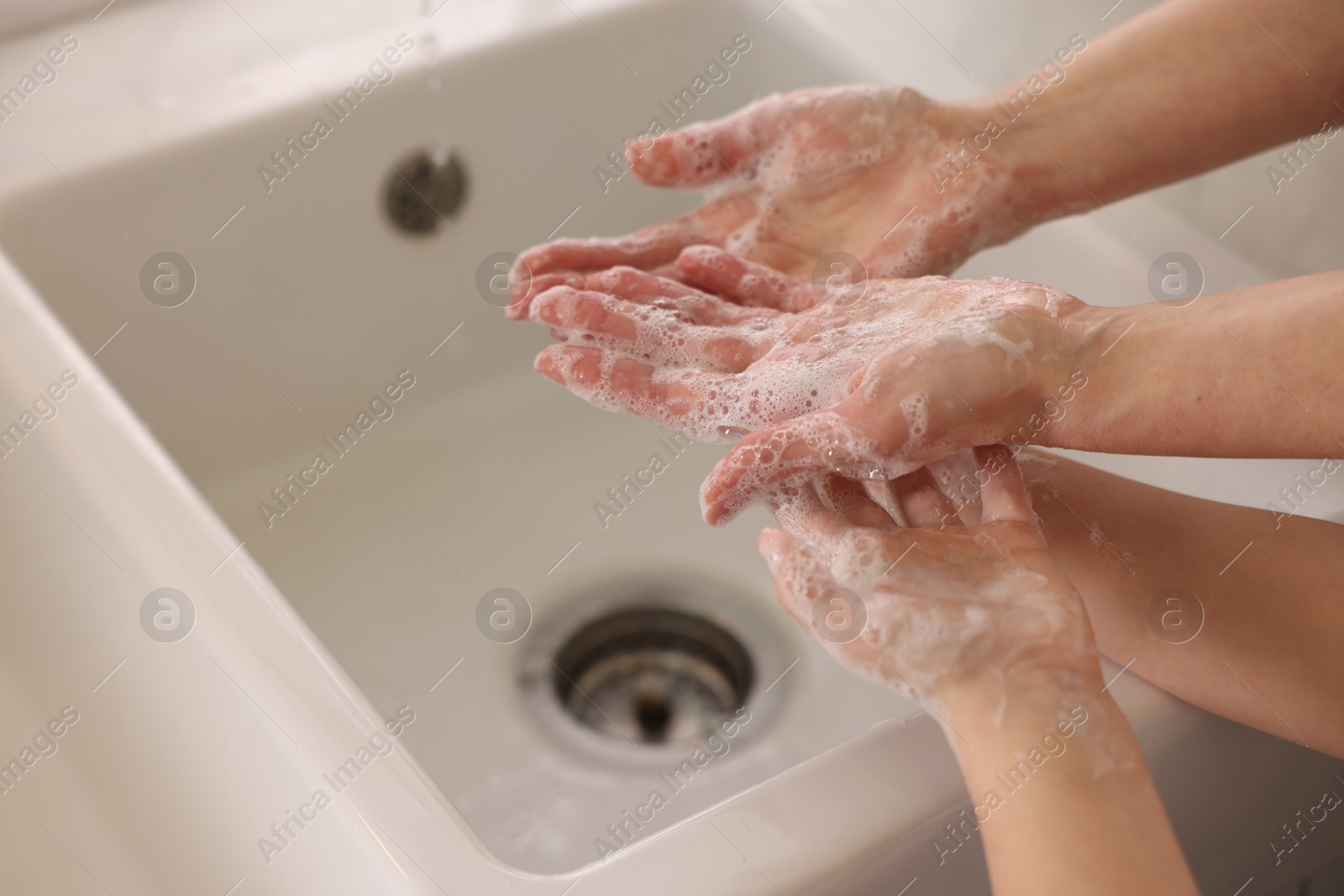 Photo of Mother and daughter washing their hands indoors, closeup