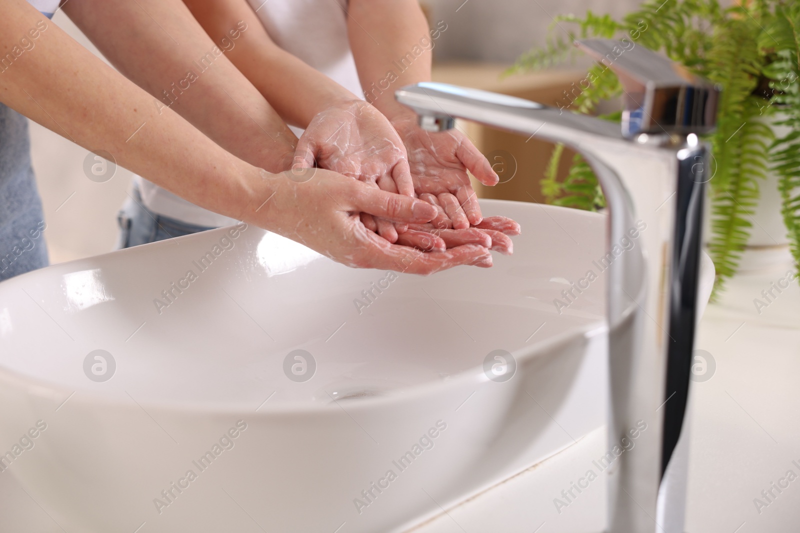 Photo of Mother and daughter washing their hands above sink indoors, closeup