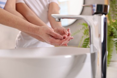 Photo of Mother and daughter washing their hands above sink indoors, closeup