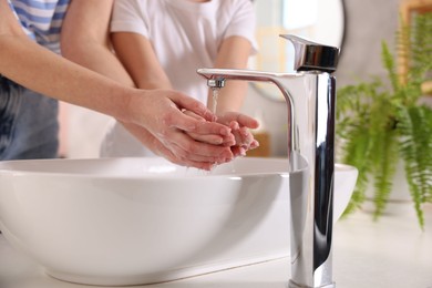 Photo of Mother and daughter washing their hands above sink indoors, closeup