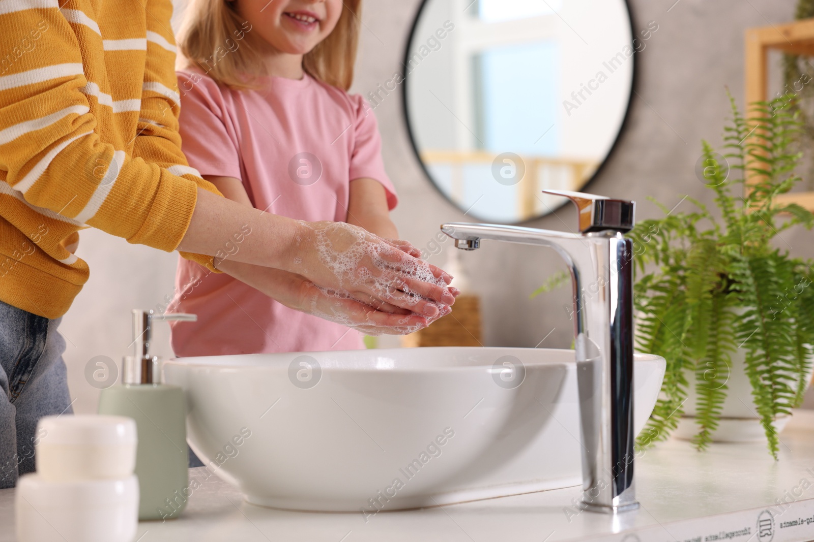 Photo of Mother and daughter washing their hands above sink indoors, closeup