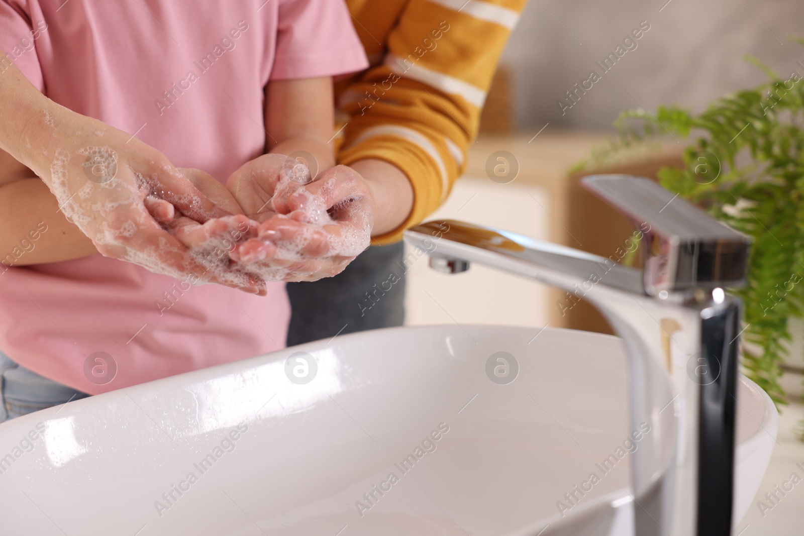 Photo of Mother and daughter washing their hands above sink indoors, closeup