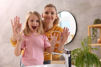 Photo of Happy mother and daughter washing their hands in bathroom