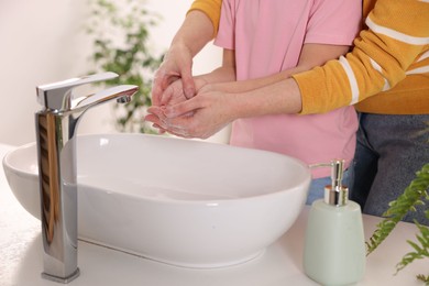 Photo of Mother and daughter washing their hands above sink indoors, closeup