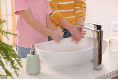 Photo of Mother and daughter washing their hands above sink indoors, closeup