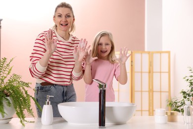 Photo of Happy mother and daughter washing their hands at home. Space for text