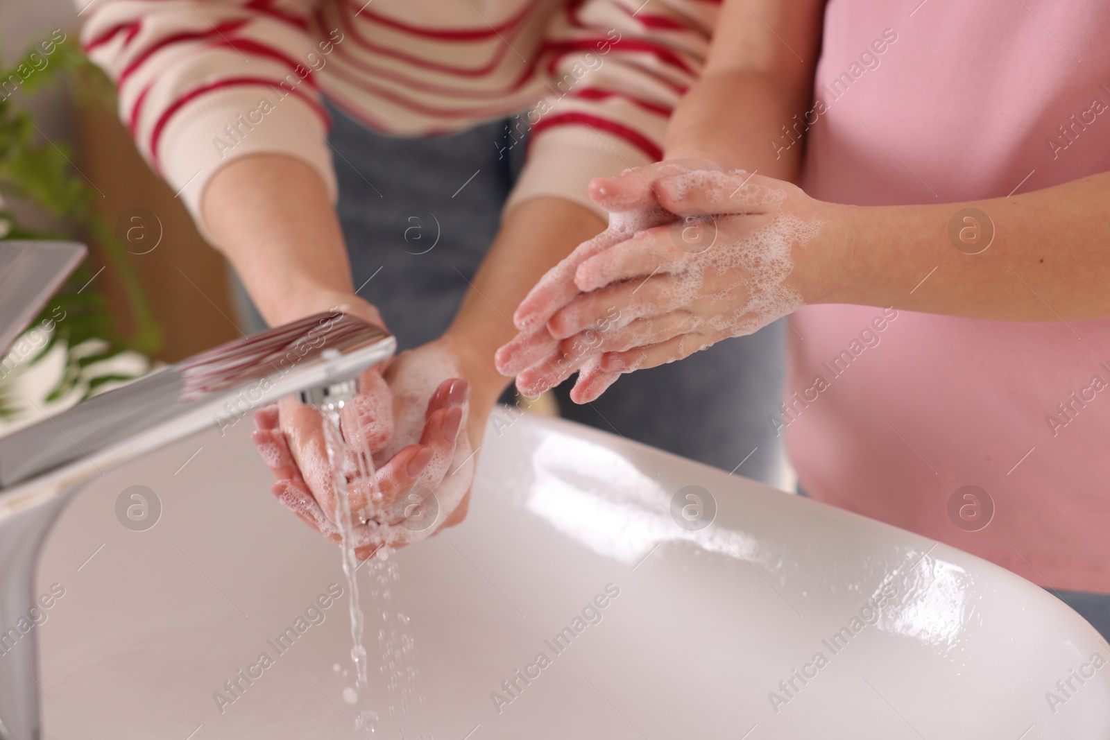 Photo of Mother and daughter washing their hands above sink indoors, closeup