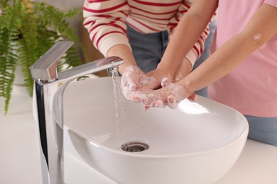 Photo of Mother and daughter washing their hands above sink indoors, closeup