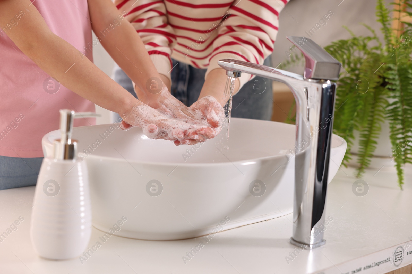 Photo of Mother and daughter washing their hands above sink indoors, closeup