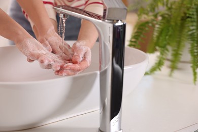 Photo of Mother and daughter washing their hands above sink indoors, closeup