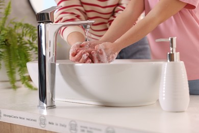 Photo of Mother and daughter washing their hands above sink indoors, closeup