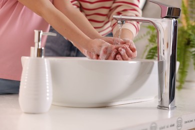 Photo of Mother and daughter washing their hands above sink indoors, closeup