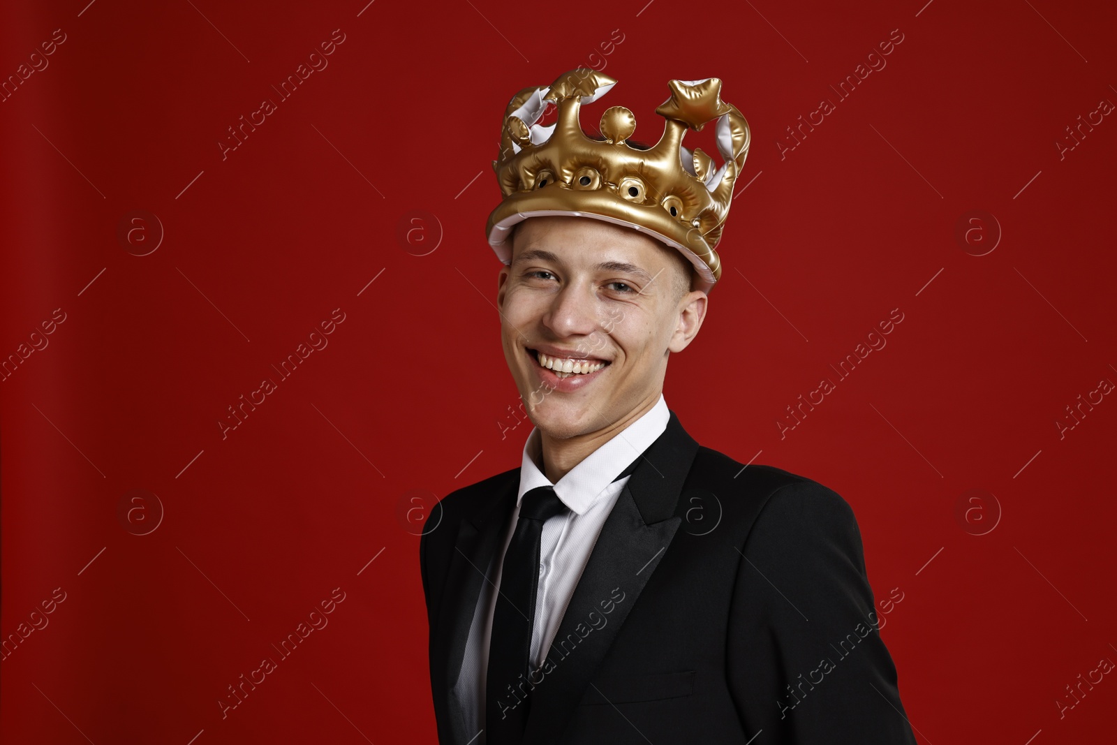 Photo of Handsome man wearing inflatable crown on red background