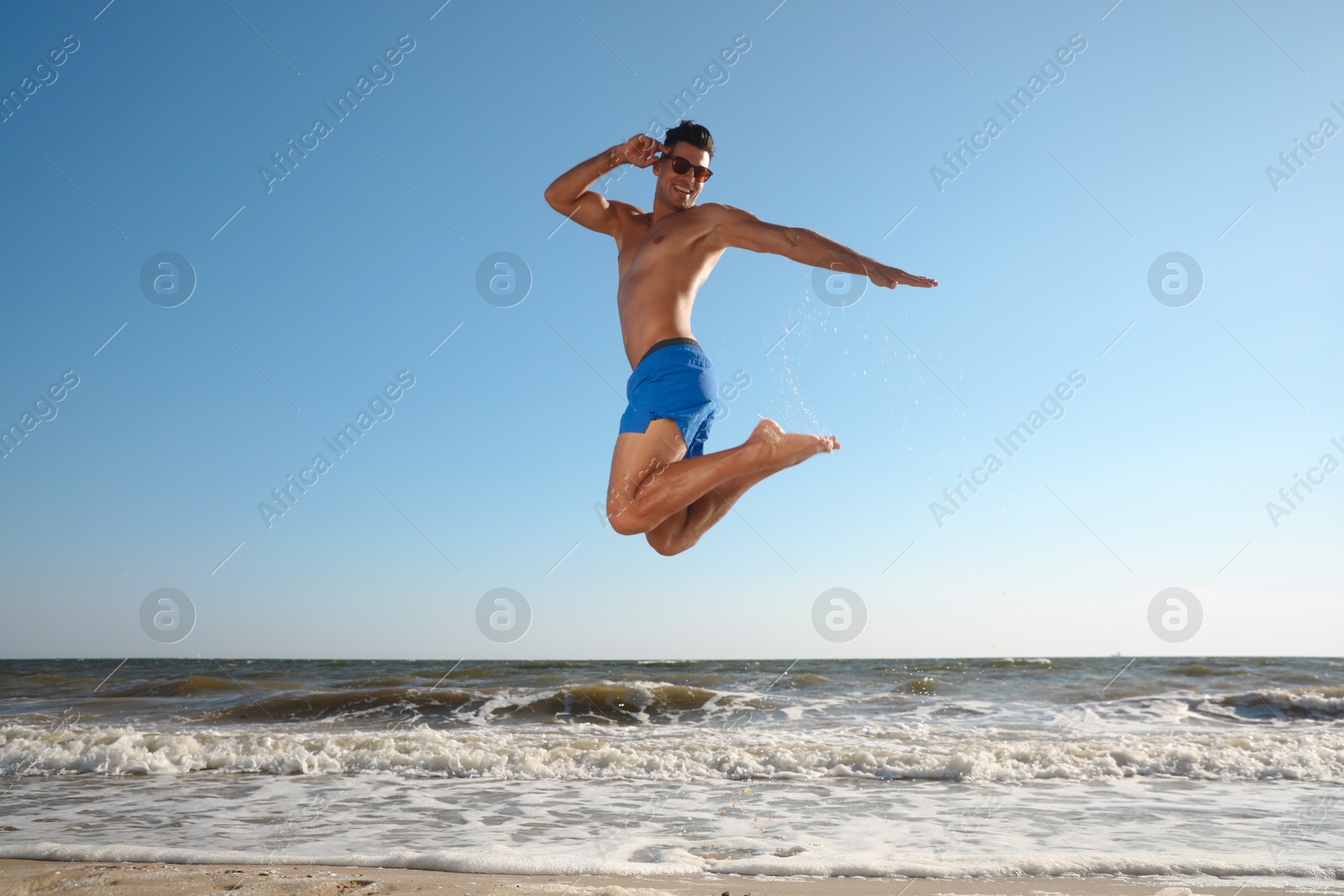 Photo of Attractive man with perfect body jumping on beach